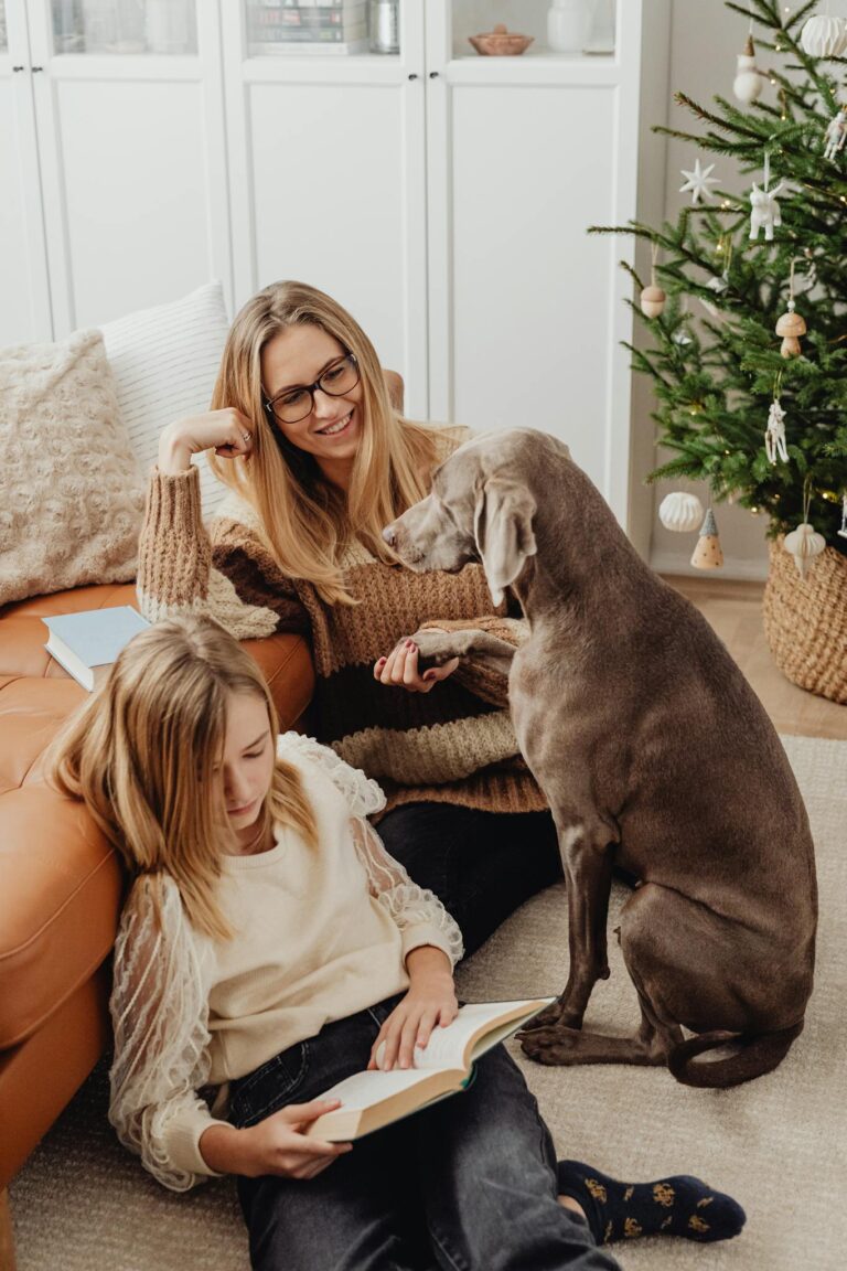 A cozy family moment with mother, daughter, and dog near a decorated Christmas tree.