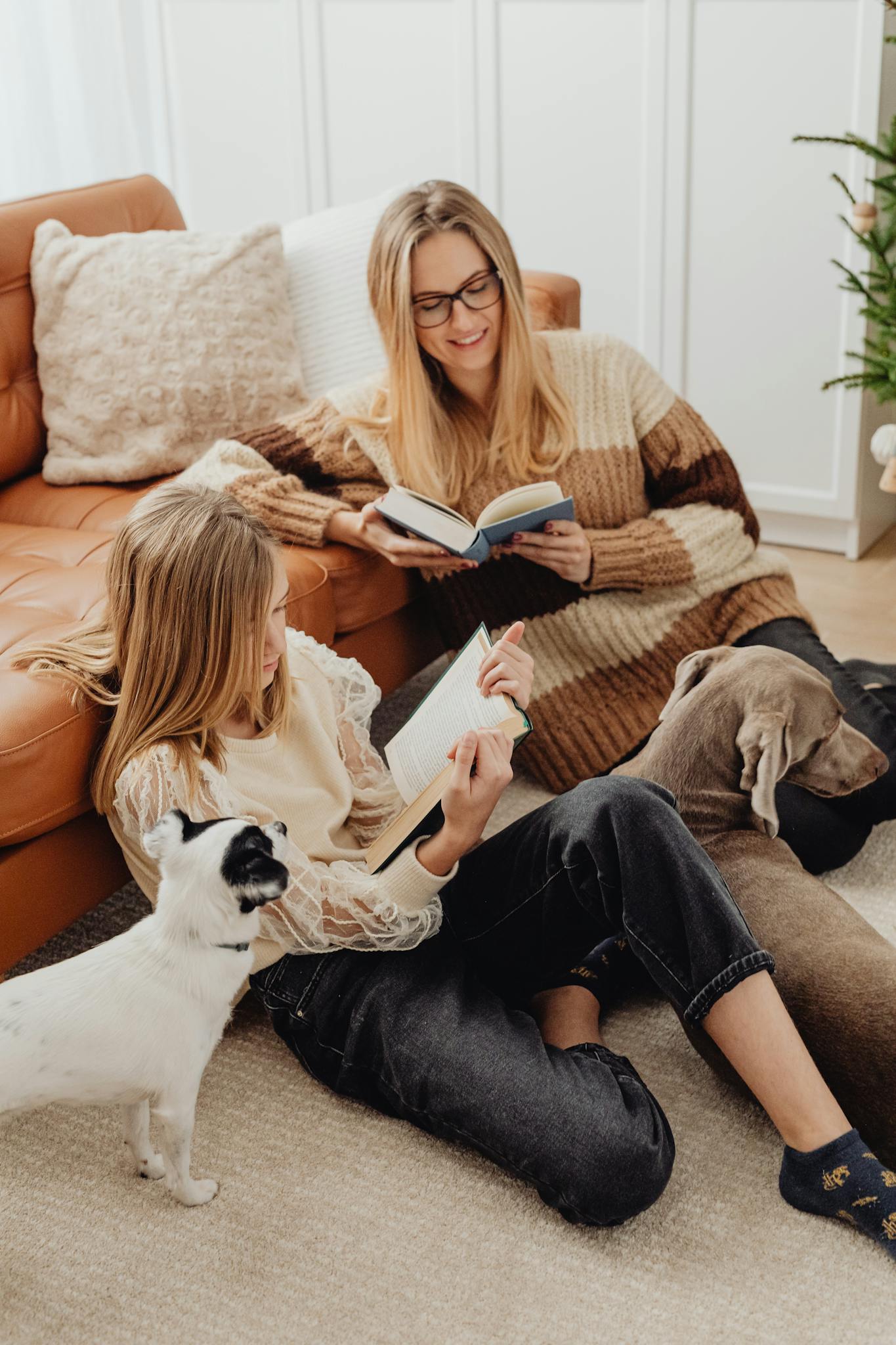 A cozy family scene with mother and daughter reading books together on the sofa with their dogs.